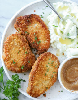 three pork chops with mashed potatoes and applesauce on white plate