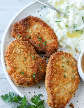 three pork chops on a white plate with parsley