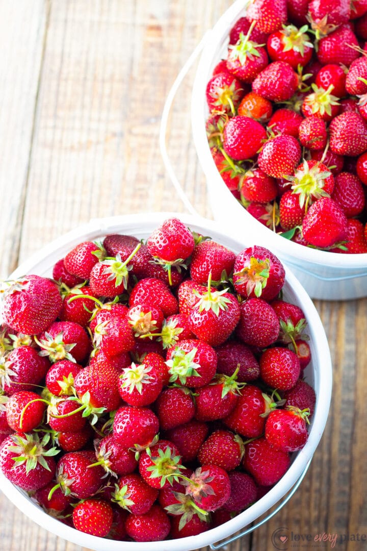 two large white buckets of strawberries