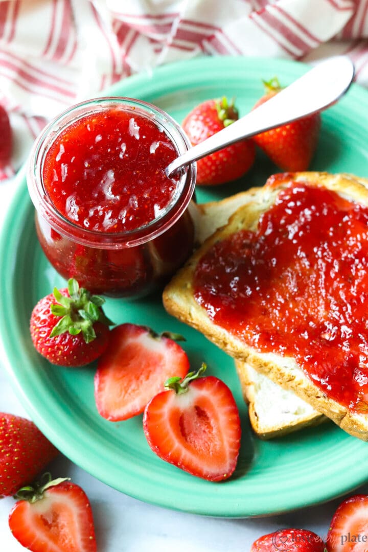 jar of strawberry jam on a green plate with bread and strawberries