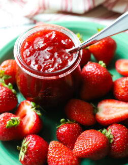 small jar of strawberry jam on a green plate with whole strawberries