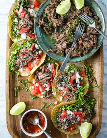 tray of tacos filled with shredded beef, tomatoes, onions, lettuce and salsa.