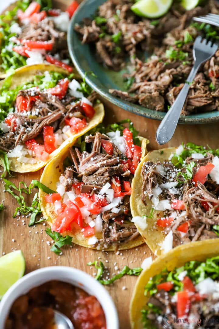 tray of corn tortillas filled with shredded beef, tomatoes, onion and lettuce.