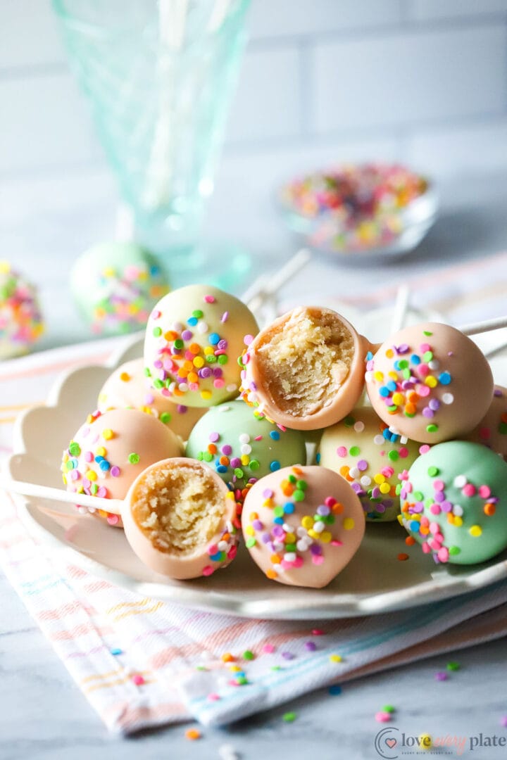 plate of cake pops with sprinkles and a striped towel underneath the plate