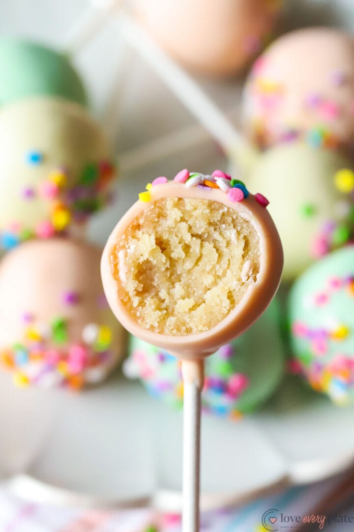 cake pop that has been bitten with a plate of other cake pops in the background