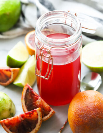 jar of red simple syrup with limes and orange slices