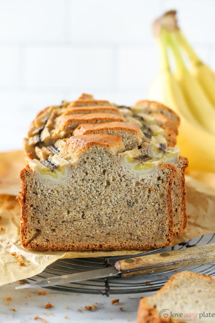 banana bread slices with bananas behind the loaf and knife in front