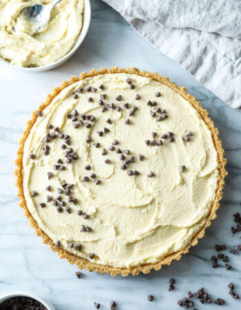 top view of cannoli tart with chocolate chips and a small bowl of cream set to the side