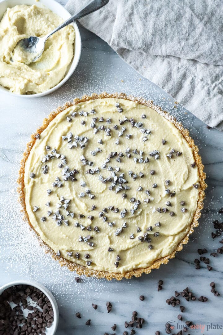 top view of a cannoli tart, garnished with chocolate chips and powdered sugar.