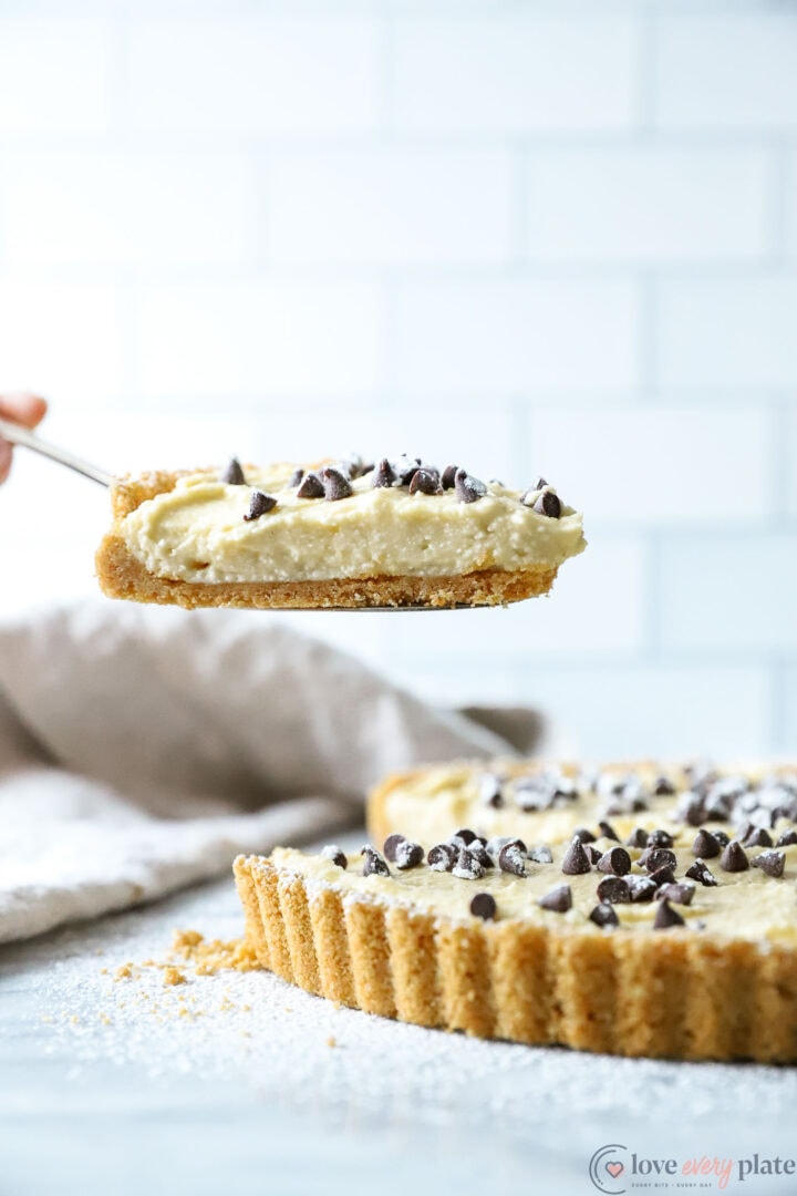 a whole cannoli tart with a slice being lifted from it.