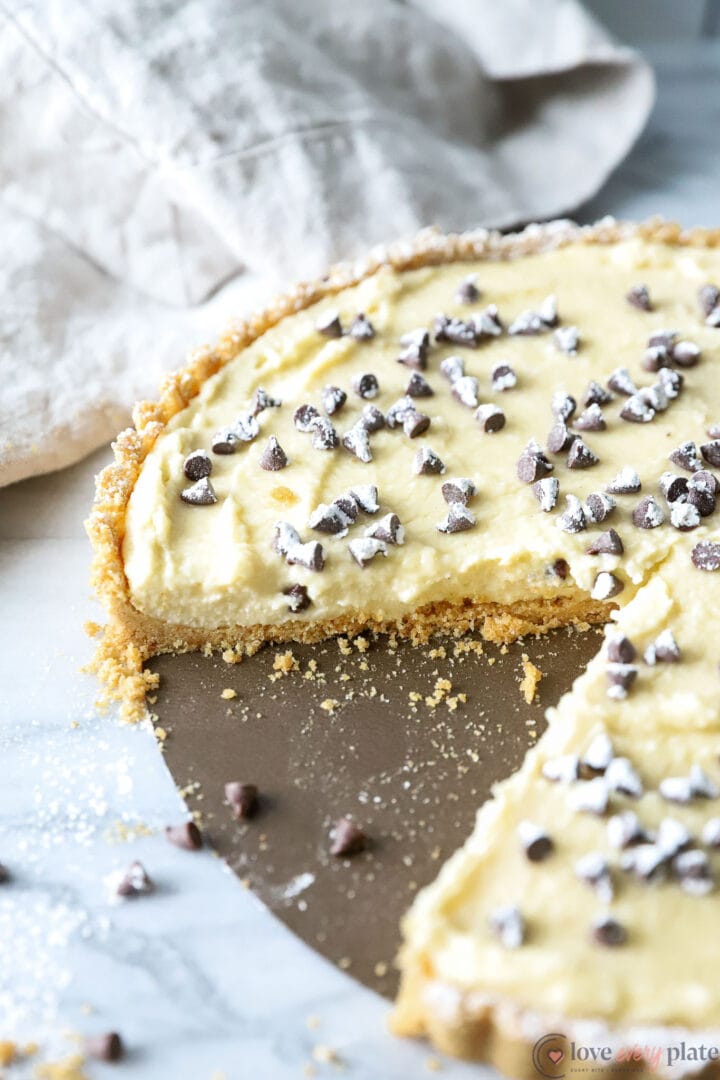 a sliced cream tart garnished with chocolate chips and powdered sugar