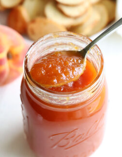 jar of peach preserves with a spoon resting on top of the jar