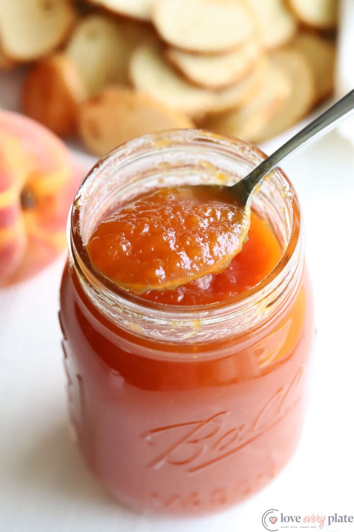 jar of peach preserves with a spoon resting on top of the jar