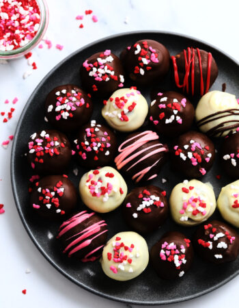 dark plate of red velvet cake balls, covered in valentine's heart sprinkles.