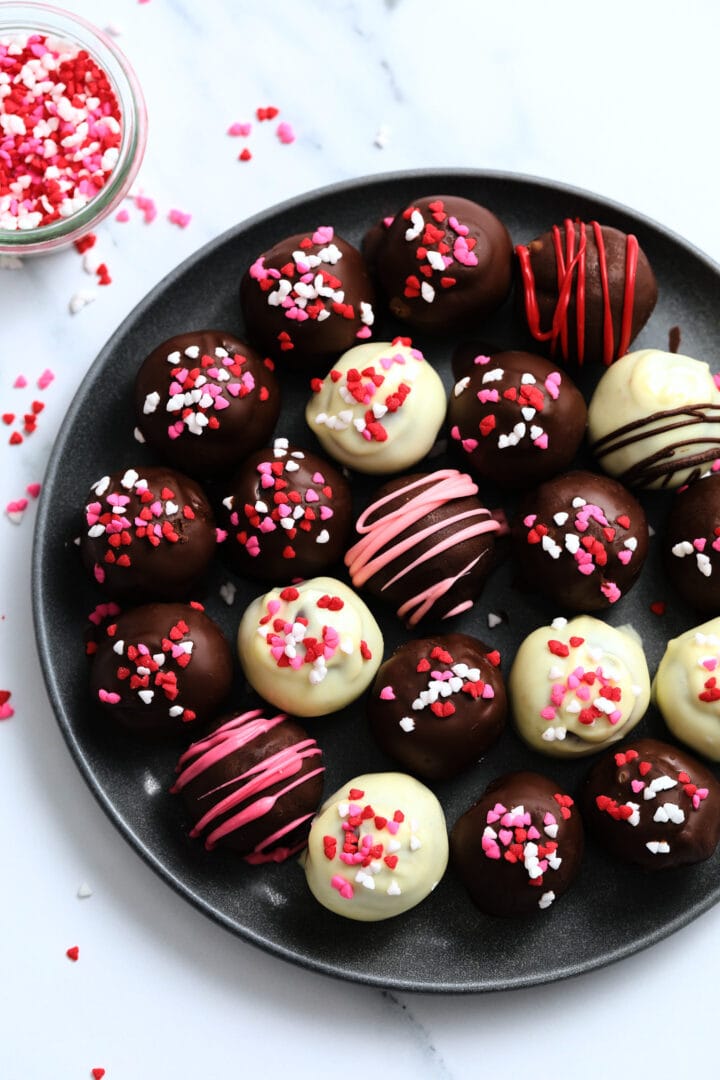 dark plate of red velvet cake balls, covered in valentine's heart sprinkles.