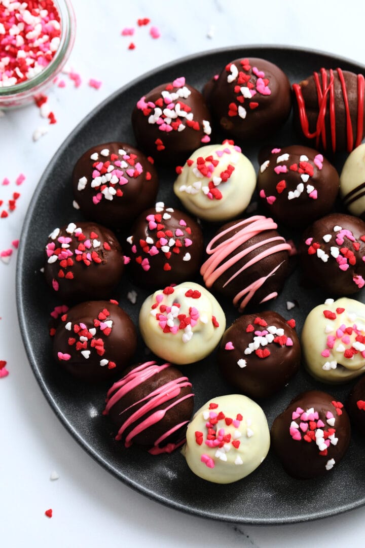 dark plate of red velvet cake balls, covered in valentine's heart sprinkles.