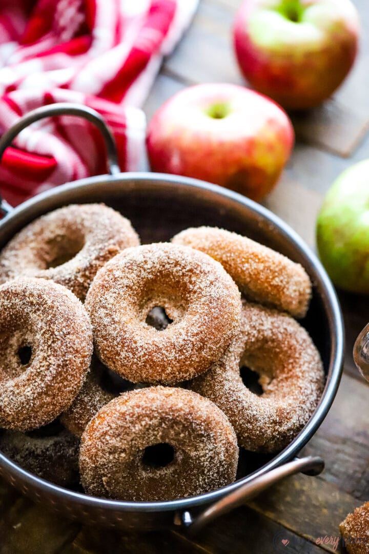 copper bowl of cinnamon sugar dusted donuts with apples in the background