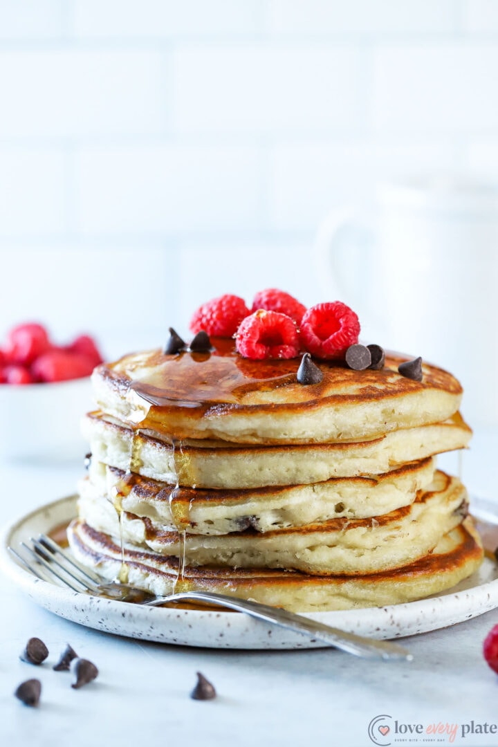 stack of chocolate chip pancakes with raspberries on top.
