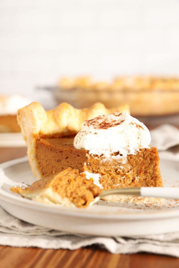 slice of pumpkin pie with a bite missing on a white plate