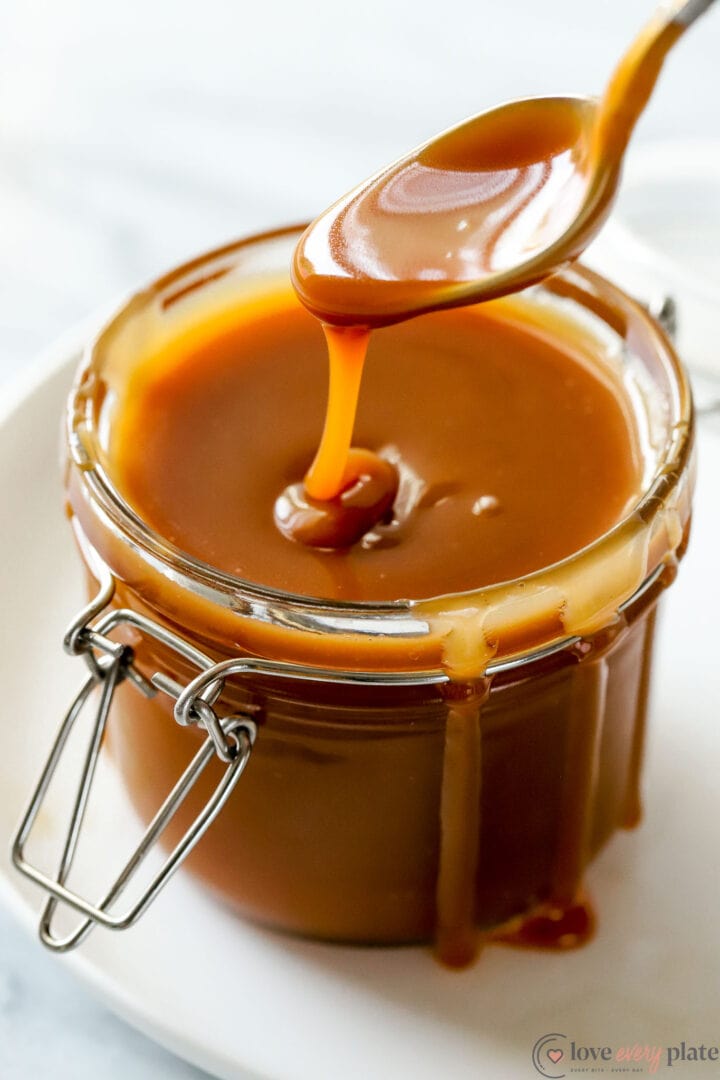 small jar of caramel sauce with a spoon drizzling caramel onto the surface.