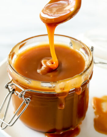 small jar of caramel sauce with a spoon drizzling caramel onto the surface.