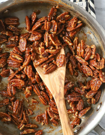 skillet of spiced pecans with a wooden spoon