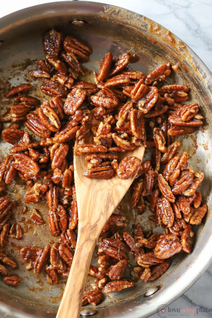 skillet of spiced pecans with a wooden spoon