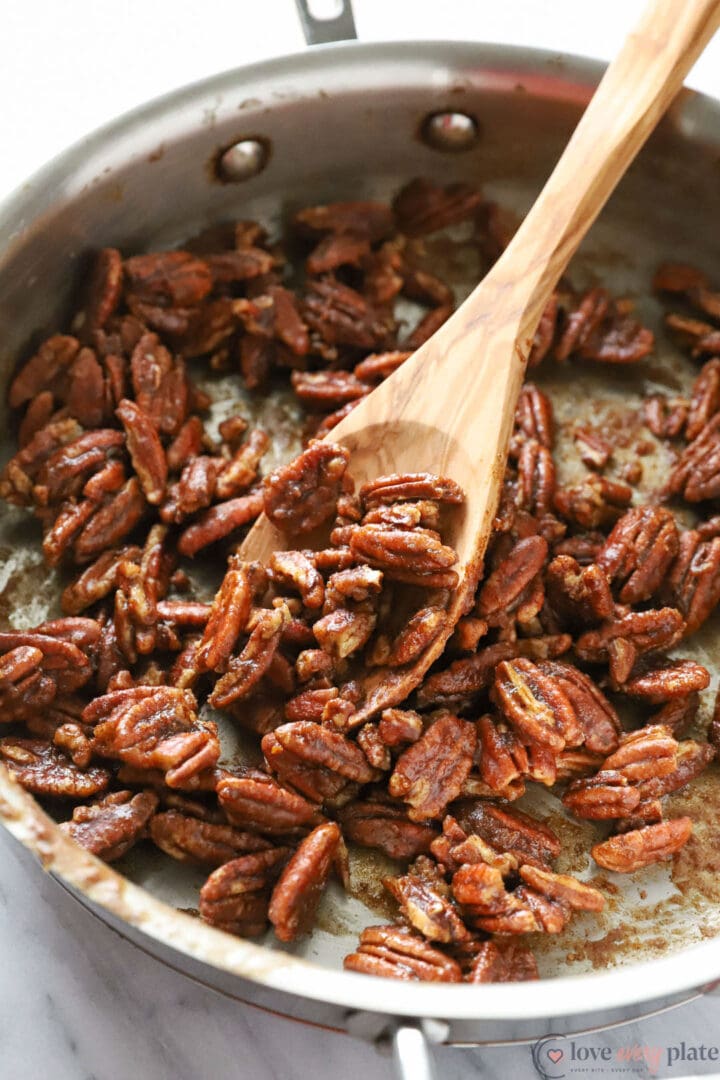 skillet of spiced pecans with a wooden spoon