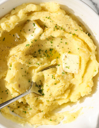 white bowl of mashed potatoes with melted butter, black pepper and chives