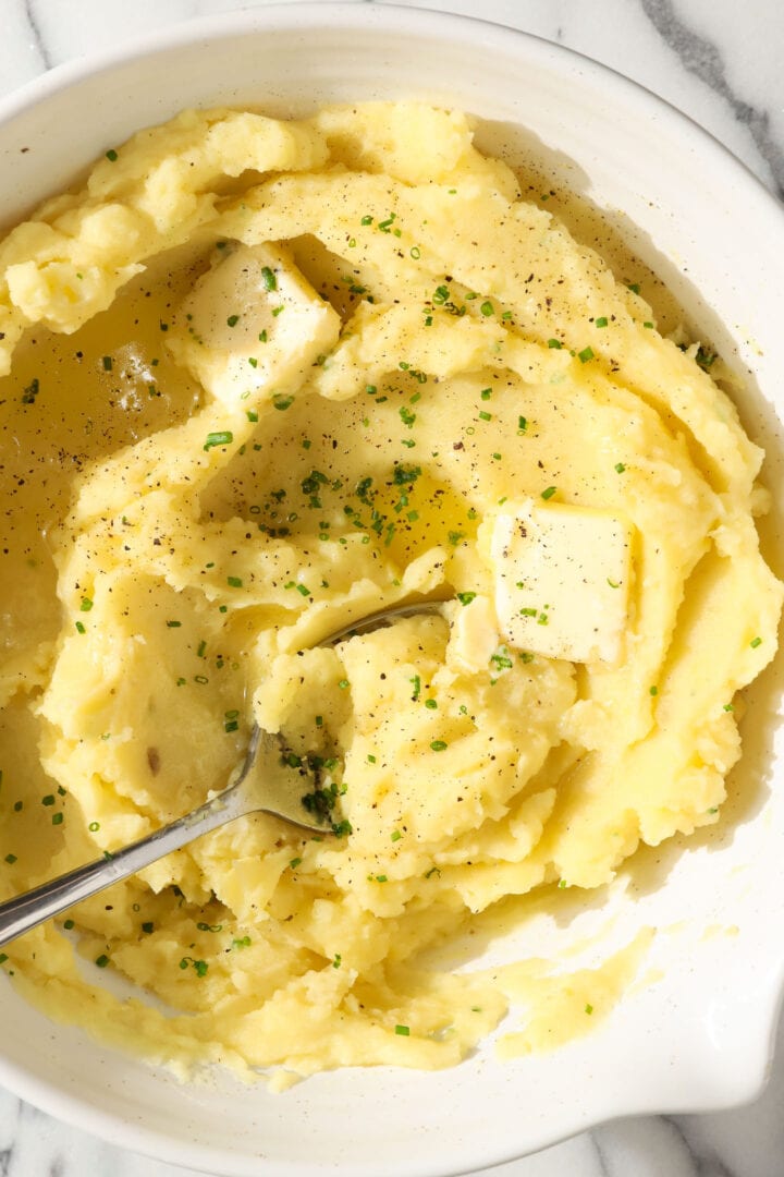 white bowl of mashed potatoes with melted butter, black pepper and chives