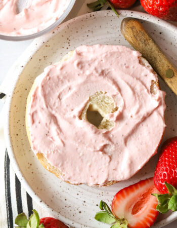 bagel half with strawberry cream cheese spread over the cut side on a white plate