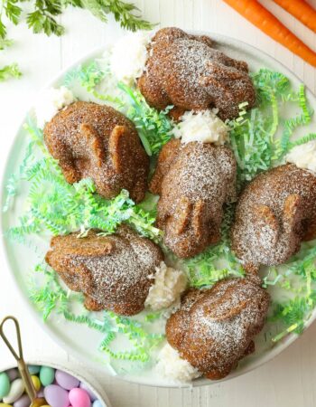 six small cakes shaped like rabbits on green paper grass and white platter