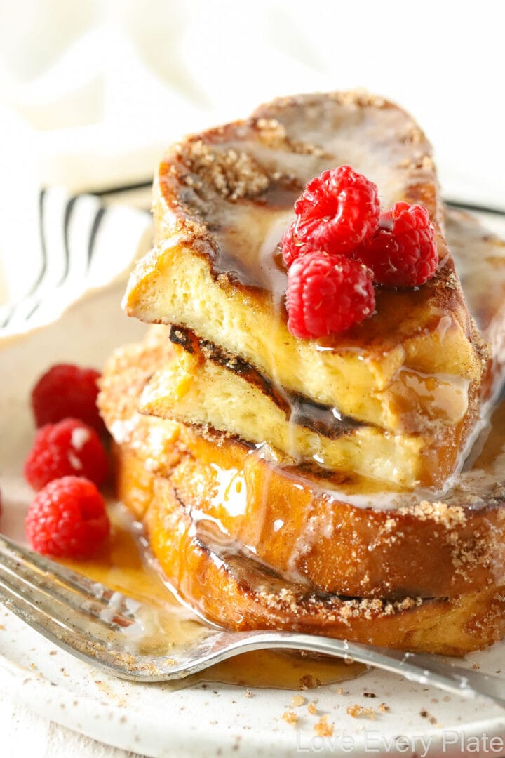 pieces of french toast drizzled with white glaze on a white oval plate with raspberries