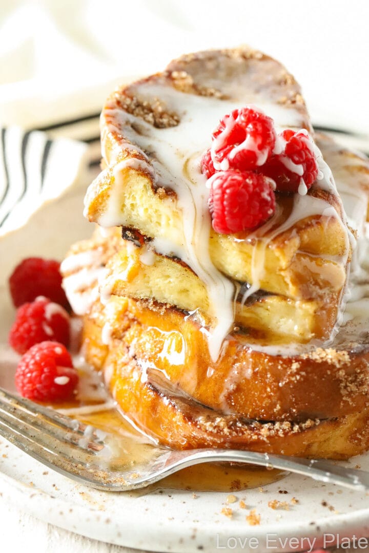 pieces of french toast drizzled with white glaze on a white oval plate with raspberries