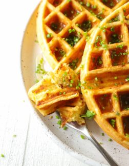 a bite of waffle next to a whole waffle on a white plate