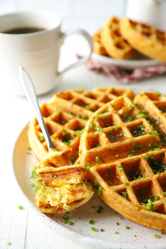 a bite of waffle on a fork on a white plate with a whole waffle