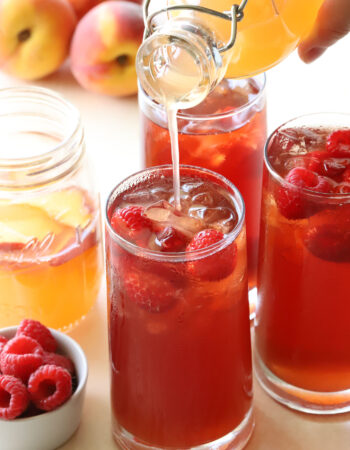 glasses of raspberry tea with peach syrup being poured into them