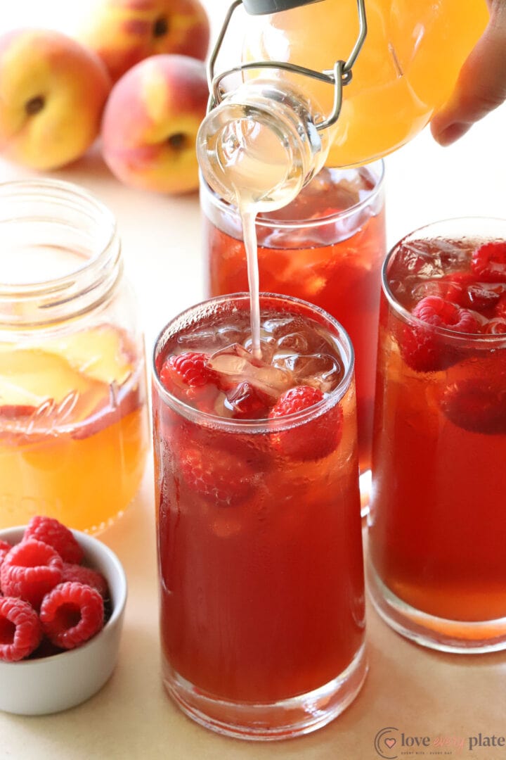 glasses of raspberry tea with peach syrup being poured into them