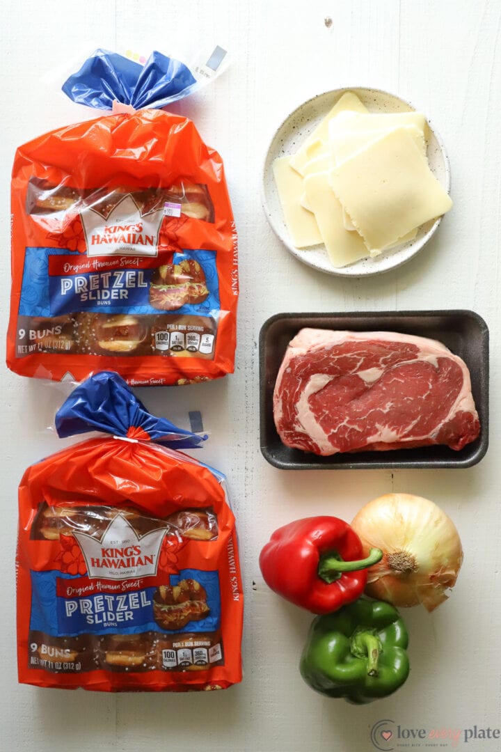 separate ingredients of steak, pretzel buns, green and red pepper and onion