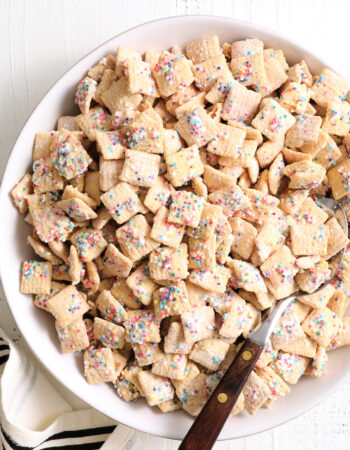 white bowl of rainbow sprinkle cereal snack, there is a wood handled spoon in the bowl.