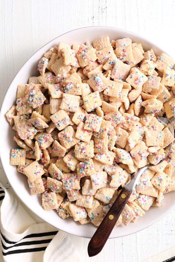 white bowl of rainbow sprinkle cereal snack, there is a wood handled spoon in the bowl.