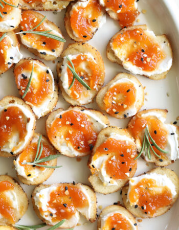 peach and goat cheese crostini on a white plate and rosemary leaves