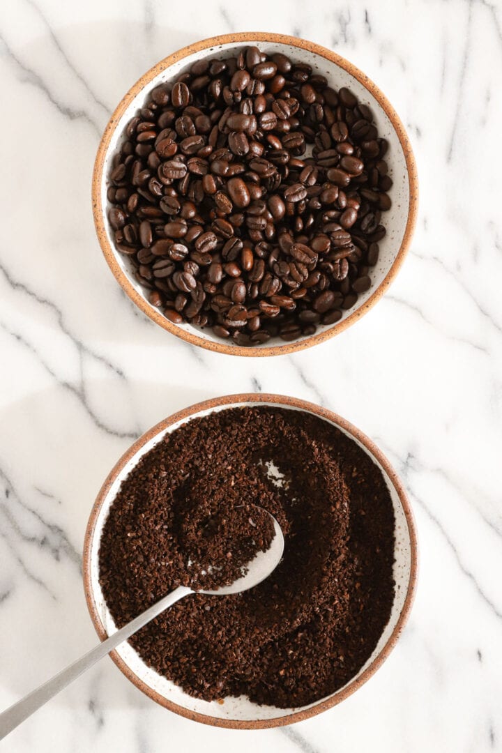 two small white bowls beside each other, one has whole coffee beans, and the other has coffee grounds