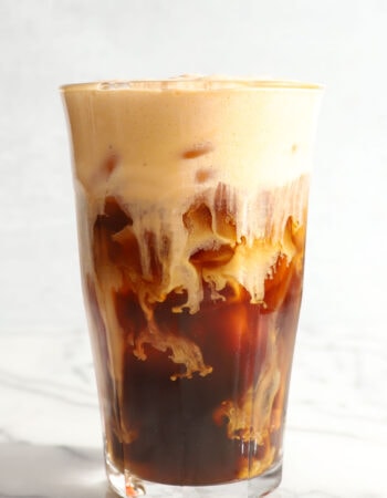 tall clear glass of cold brew coffee with pumpkin foam on top