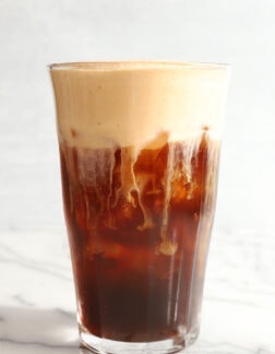 tall clear glass of cold brew coffee with pumpkin foam on top