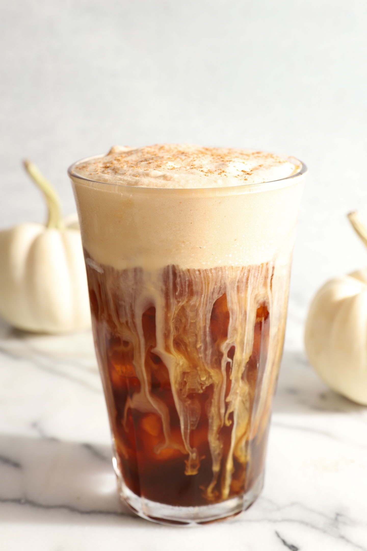 tall clear glass of cold brew coffee with pumpkin foam on top