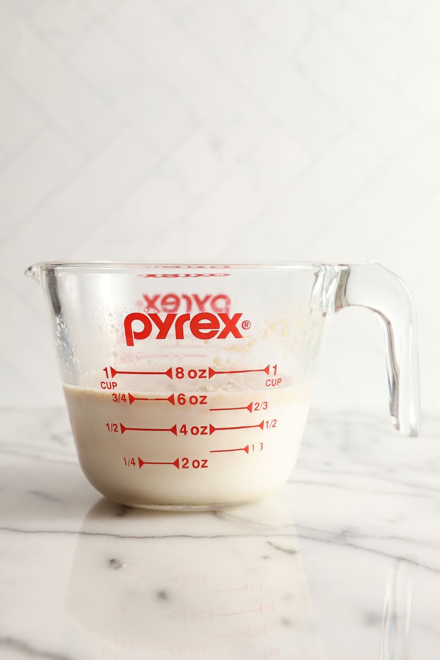 front view of a pyrex measuring cup with milk and yeast that has not yet proofed