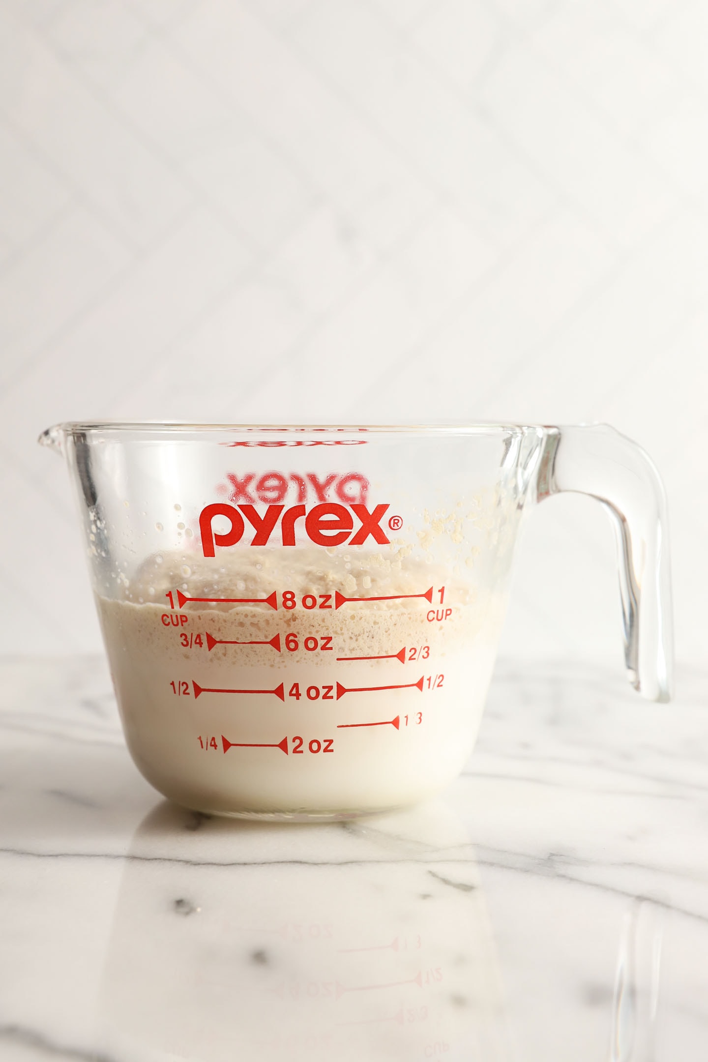 front view of a pyrex measuring cup with milk and yeast that has proofed