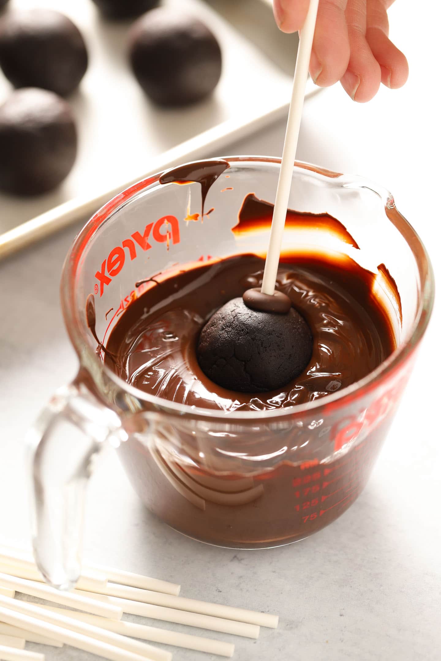 a cake pop being dipped into a cup of melted chocolate