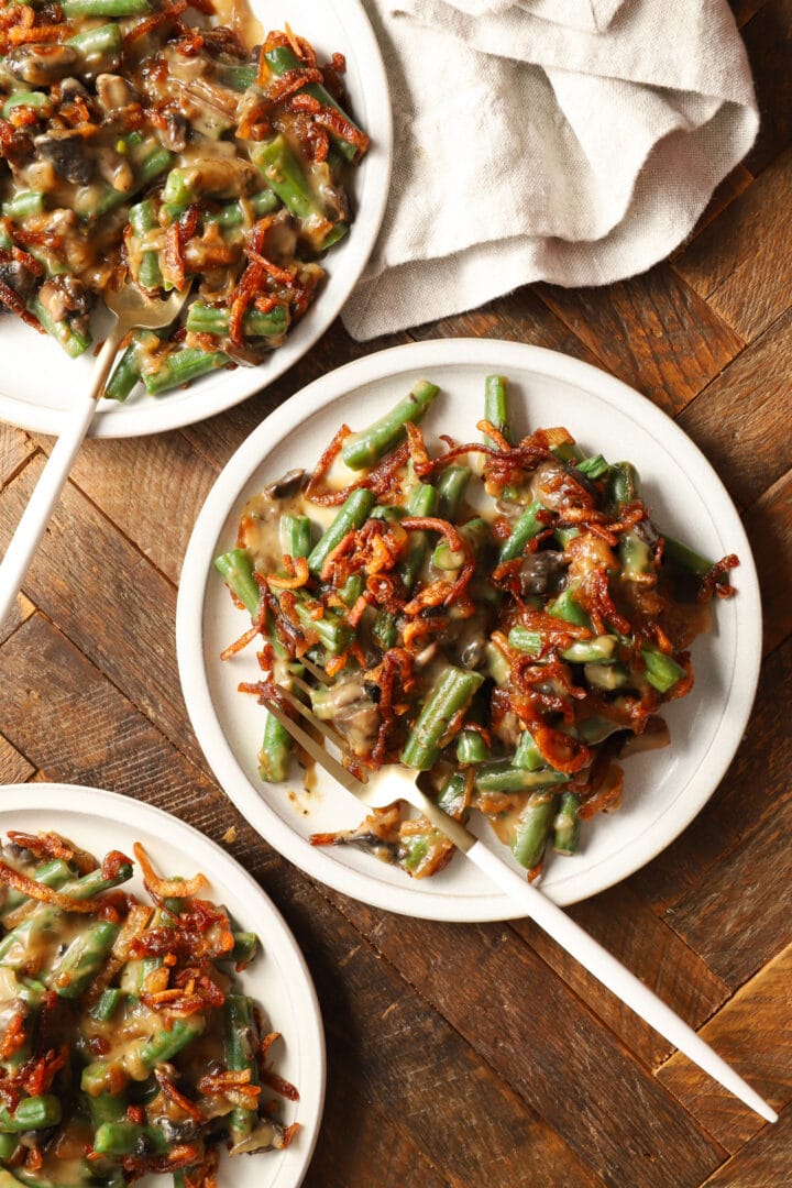 three small white plates with portions of green bean casserole and forks